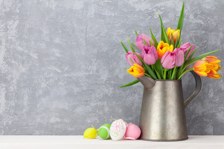 Easter eggs and colorful tulips bouquet on shelf in front of stone wall. View with copy spaceの写真素材