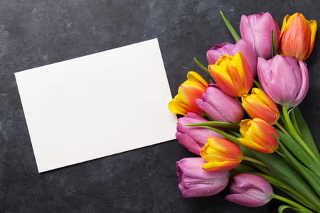 Fresh colorful tulip flowers and blank greeting card on dark stone table. Top view with copy spaceの写真素材