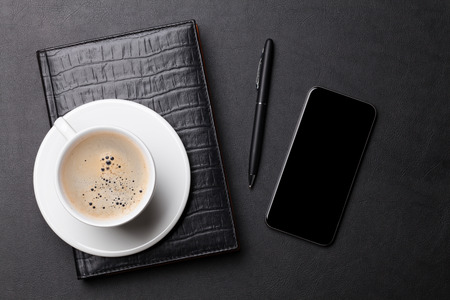 Office leather desk table with coffee cup, notepad, smartphone and pen. Top view with copy space