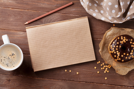 Notepad, donuts and coffee on wooden table. Top view with copy spaceの写真素材