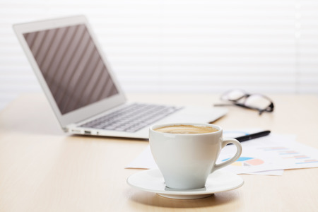 Office workplace with with laptop and coffee cup on wooden desk table in front of window with blindsの写真素材