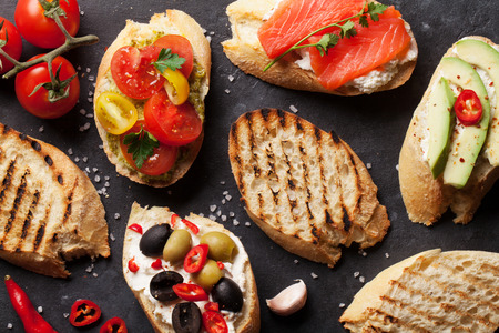 Toast sandwiches with avocado, tomatoes, salmon and olives on stone background. Top view
