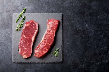 Raw striploin steak with rosemary cooking over stone table. Top view with copy spaceの写真素材
