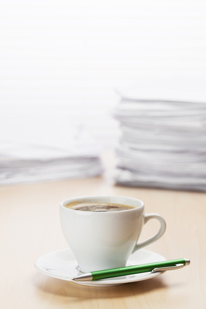 Office workplace with coffee cup and lot of documents on wood desk table in front of window with blinds. View with copy spaceの写真素材