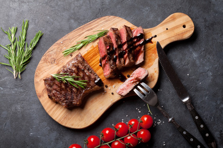 Grilled striploin sliced steak on cutting board over stone table. Top viewの写真素材