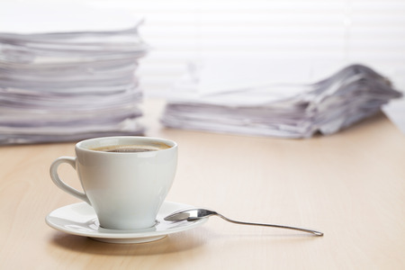 Office workplace with coffee cup and lot of documents on wood desk table in front of window with blindsの写真素材