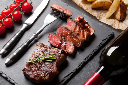 Grilled striploin sliced steak with potato and red wine over stone tableの写真素材