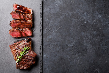 Grilled sliced beef steak with balsamico and rosemary on stone table. Top view with copy space