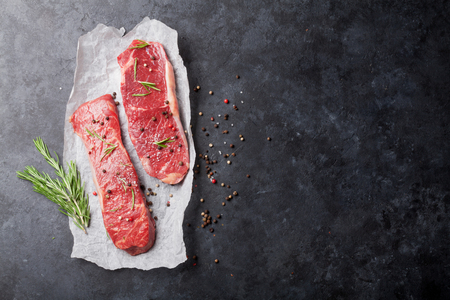 Raw striploin steak with rosemary, salt and pepper cooking over stone table. Top view with copy spaceの写真素材