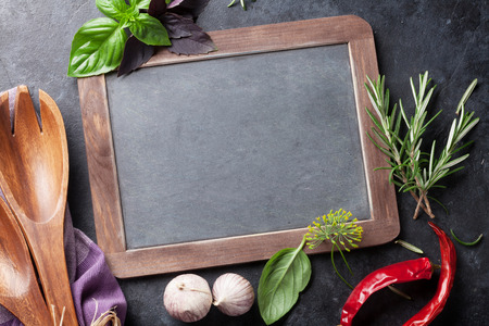 Blackboard for your text, fresh garden herbs and spices on stone table. Basil, rosemary, dill. Cooking ingredients. Top view with copy spaceの写真素材
