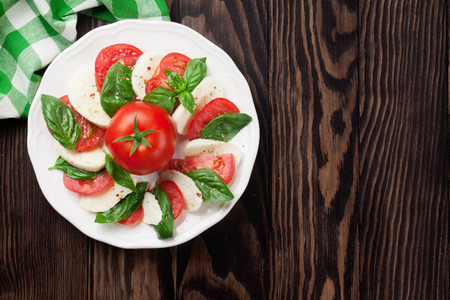 Caprese salad. Mozzarella cheese, tomatoes and basil herb leaves on plate over wooden table. Top view with copy spaceの写真素材