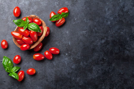 Cherry tomatoes and basil herb leaves over stone table. Top view with copy spaceの写真素材