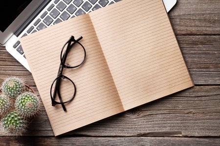Notepad for your text, glasses and laptop over wooden table. Top view with copy spaceの写真素材