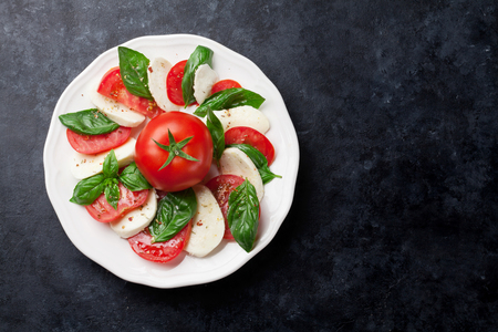 Caprese salad. Mozzarella cheese, tomatoes and basil herb leaves on plate over stone table. Top view with copy spaceの写真素材
