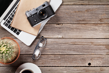 Desk table with laptop, camera, coffee and cactus on wooden table. Workplace. Top view with copy space.の写真素材
