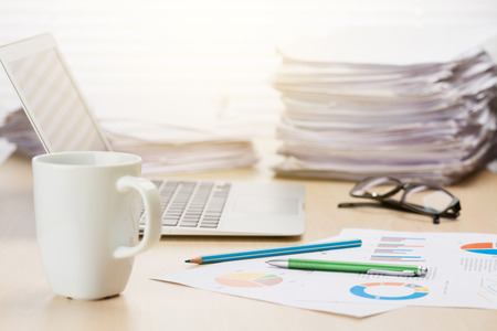 Office workplace with coffee cup, laptop and supplies on wood desk table in front of window with...
