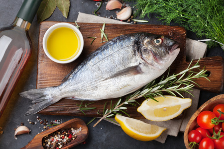 Raw fish cooking and ingredients. White wine, dorado, lemon, herbs and spices. Top view on stone tableの写真素材