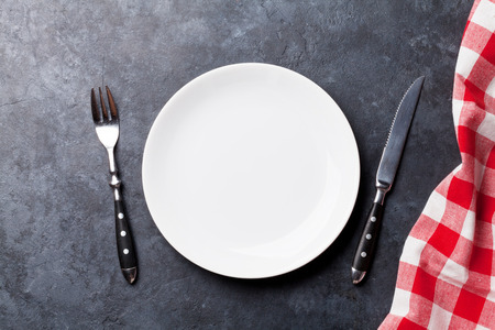 Empty plate, fork, knife and kitchen towel over stone table. Top view with copy space for your recipeの写真素材