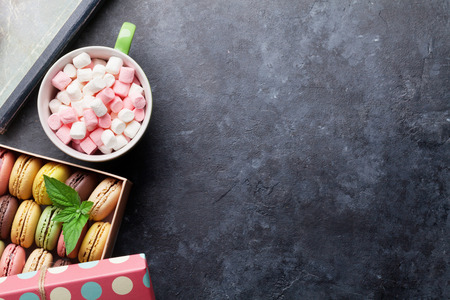 Colorful macaroons in a gift box and marshmallow in coffee cup on stone table. Top view with copy spaceの写真素材