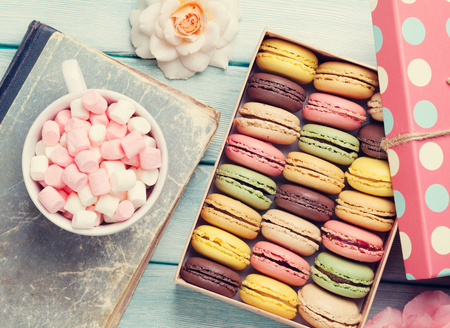 Colorful macaroons in a gift box and marshmallow in coffee cup on wooden table. Top view. Retro tonedの写真素材
