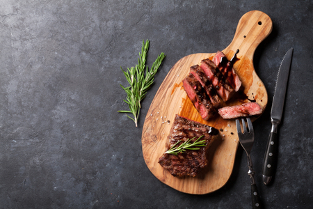 Grilled sliced beef steak on cutting board over stone table. Top view with copy spaceの写真素材