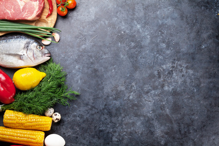 Vegetables, fish, meat and ingredients for cooking. Tomatoes, pepper, corn, beef, eggs. Top view with copy space on stone tableの写真素材