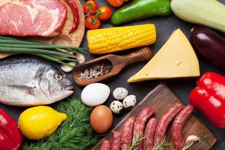 Vegetables, fish, meat and ingredients for cooking. Tomatoes, pepper, corn, beef, eggs. Top view on stone tableの写真素材
