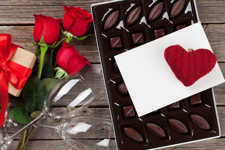 Valentines day greeting card. Red roses, chocolate sweets gift box and wine glasses on wooden table. Top viewの写真素材