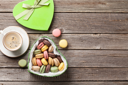 Colorful macaroons in Valentines day heart shaped gift box and coffee cup on wooden table. Top view with copy spaceの写真素材