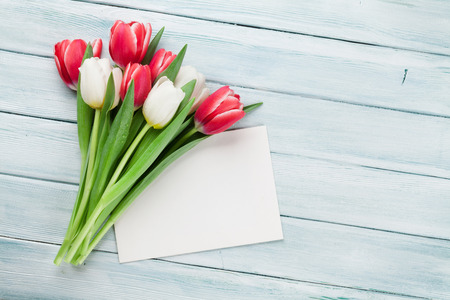 Colorful tulips bouquet on wooden background. Red and white. Top view with greeting card for textの写真素材