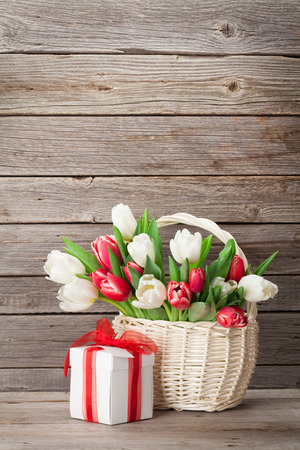 Colorful tulips bouquet and gift box in front of wooden wall. Red and white. With space for greetingsの写真素材