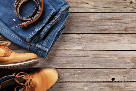 Men's clothes and accessories. Jeans, shoes and belt on wooden background. Top view with copy spaceの写真素材