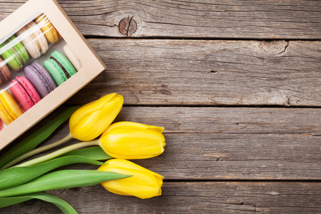Colorful macaroon cookies and yellow tulips bouquet on wooden table. Top view with copy spaceの写真素材