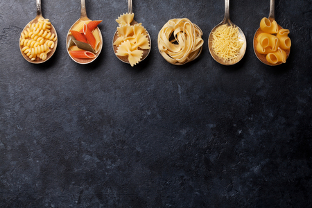 Various pasta on spoons over stone background. Top view with copy spaceの写真素材