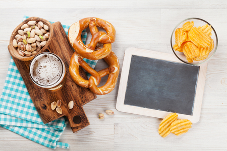 Lager beer and snacks on wooden table. Nuts, chips, pretzel. Top view with chalkboard for copy spaceの写真素材
