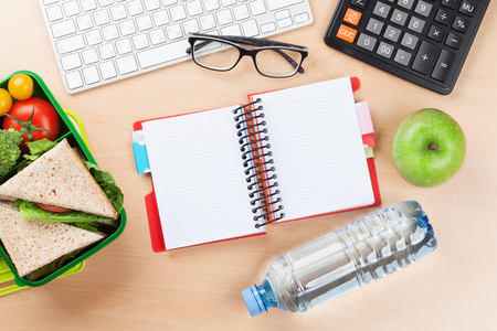 Office desk with supplies and lunch box with vegetables and sandwich. Top view with space for your textの写真素材