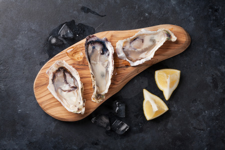 Opened oysters, ice and lemon on board over stone table. Top viewの写真素材