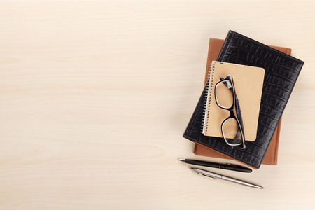 Wooden office desk with supplies. Notepad, pen and glasses. Top view with space for your text