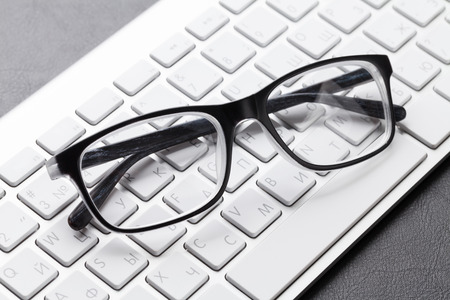 Office desk with eyeglasses over computer keyboardの写真素材