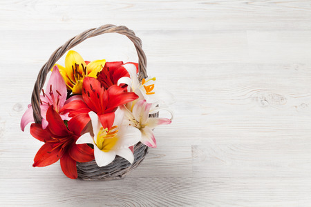 Colorful lily flowers in basket on wooden background with space for your greetingsの写真素材