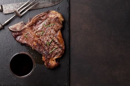 Grilled T-bone steak and red wine glass on stone table. Top view with copy space