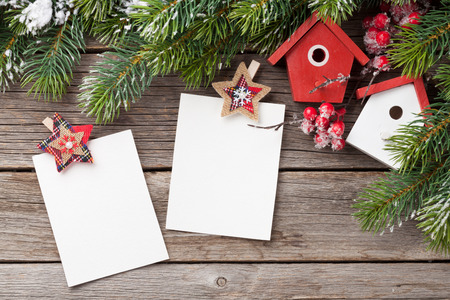 Christmas blank photo frames, birdhouse decor and snow fir tree on wooden table. Top view with space for your greetingsの写真素材