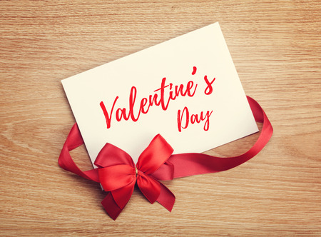 Valentine's day blank gift card and red ribbon with bow on wooden backgroundの写真素材