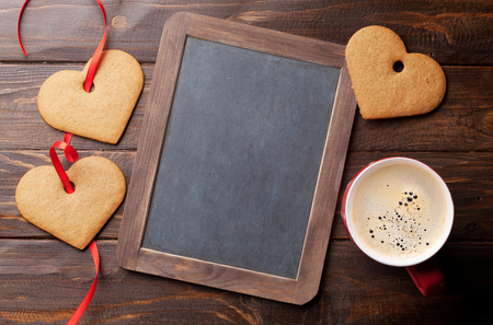Valentines day greeting card with heart cookies and coffee cup on wooden table. With chalkboard for your greetingsの写真素材