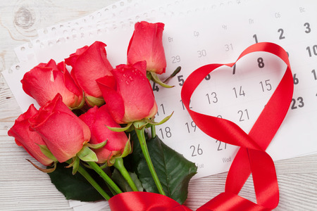Valentines day greeting card with red roses and heart shaped ribbon over february calendar on wooden background. Top viewの写真素材