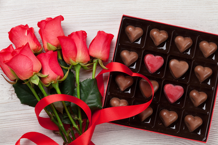 Valentines day greeting card with red roses and heart shaped chocolate on wooden background. Top viewの写真素材