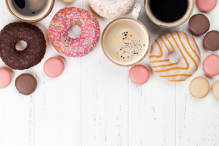 Coffee cups, donuts and macaroons on white wooden table. Top view with space for your textの写真素材