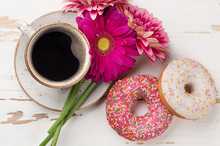 Coffee cup, donuts and gerbera flowers on white wooden table. Top viewの写真素材