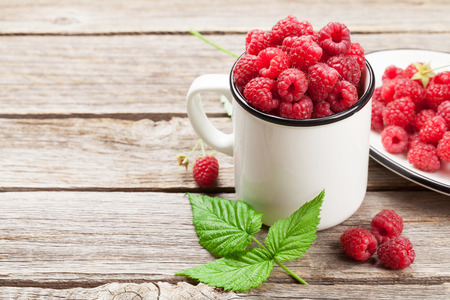 Cup of ripe raspberries on wooden table. With space for your text