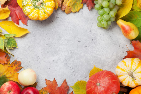 Autumn backdrop with pumpkins, apples, pears, grapes and colorful leaves over stone background. Top...